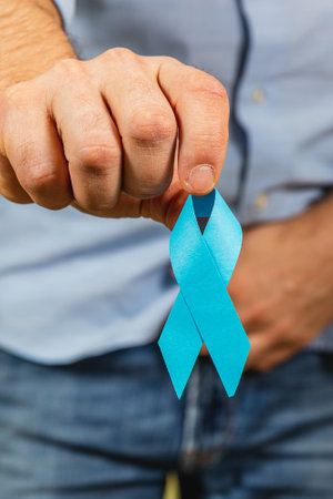 A man holds a blue awareness ribbon to promote men's health issues, including prostate cancer. This campaign aims to increase awareness and encourage support for prevention initiatives.の写真素材