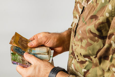 A soldier in camouflage attire counts different banknotes, showcasing a moment of financial transaction, possibly during duty or personal time.の写真素材
