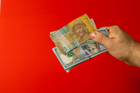 A hand holds various banknotes, showcasing both local and foreign currencies against a vibrant red background, illustrating the concept of money exchange.の写真素材