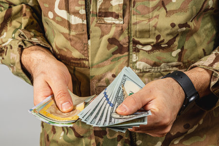 A soldier checks the cash in hand while wearing military attire, showing a mixture of bills in various denominations under casual lighting conditions.の写真素材