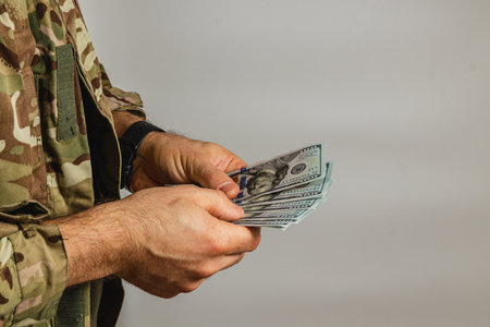 A soldier in a camouflage uniform counts several banknotes, highlighting the contrast between...