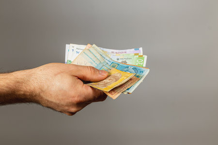A hand extends, displaying a mix of banknotes of different denominations, showcasing the diversity of currency. The background is plain, emphasizing the money.の写真素材