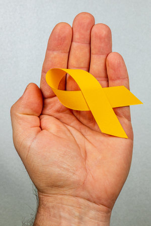 A hand holds a yellow ribbon representing solidarity and hope for those battling cancer. This symbol highlights awareness, courage, and the importance of early detection.の写真素材