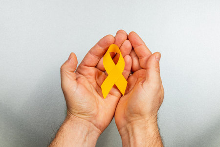 Two hands gently cradle a yellow ribbon, symbolizing hope and awareness in the fight against cancer. This image highlights the significance of solidarity and support for those affected by illness.の写真素材