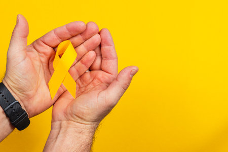 Two hands cradle a yellow ribbon, representing solidarity in the fight against cancer. This visual highlights awareness, support, and hope for those affected by illness.の写真素材