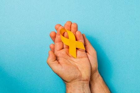 Two hands gently cradle a yellow ribbon, symbolizing hope and solidarity in the fight against cancer. This visual emphasizes awareness, care, and support for those affected.の写真素材