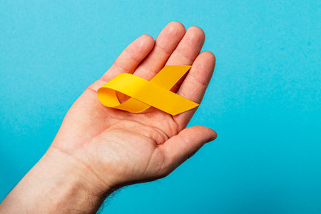 A person holds a yellow ribbon in their hand against a blue background, representing awareness and support in the fight against cancer. This symbol embodies hope and courage.の写真素材