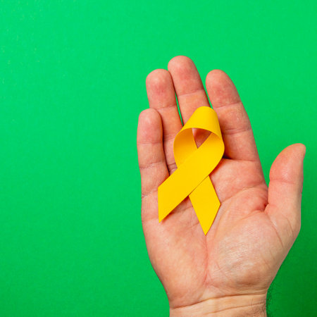 A hand holds a yellow ribbon against a green background, representing hope and support in the fight against cancer. This symbol highlights awareness and the importance of health.の写真素材