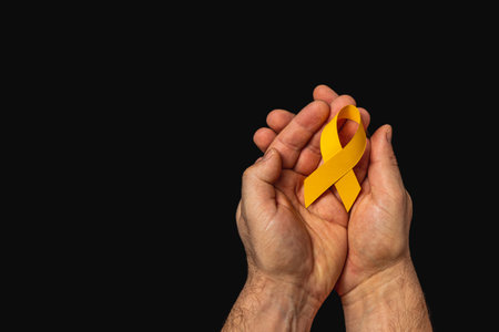 Two hands grasp a yellow ribbon, representing hope and solidarity in the fight against cancer. This powerful symbol emphasizes the importance of awareness and support for patients.の写真素材