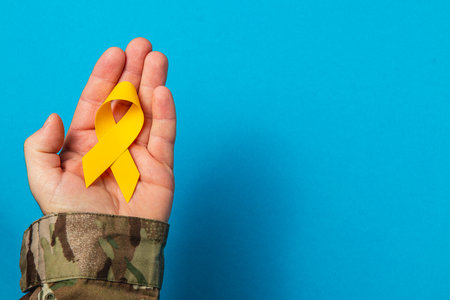 A hand holds a yellow ribbon signifying support for cancer awareness. The bright blue background enhances the symbolism of courage and solidarity in the fight against the disease.の写真素材