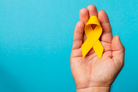 A woman's hand firmly grips a yellow ribbon, a symbol of courage and support for cancer awareness. The vibrant blue background enhances the message of solidarity and hope.の写真素材