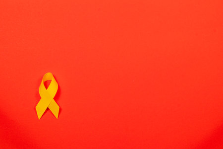 An isolated yellow ribbon rests against a vibrant red background, symbolizing solidarity and hope in the fight against cancer. This awareness campaign emphasizes the importance of care and support.の写真素材