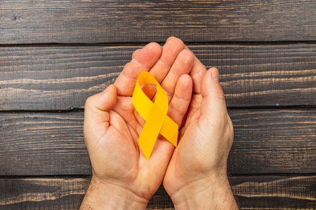 Two hands support a yellow ribbon, representing solidarity in the fight against cancer. This visual emphasizes awareness, hope, and the importance of support during diagnosis and treatment.の写真素材