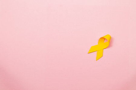 A yellow ribbon rests on a soft pink background, symbolizing awareness and support for those affected by cancer. This representation promotes courage, healing, and community solidarity.の写真素材