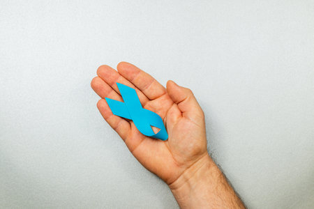 A male hand displays a blue ribbon, representing cancer awareness and support for patients fighting various types of cancer, including prostate and colon. This symbolizes hope and prevention.の写真素材