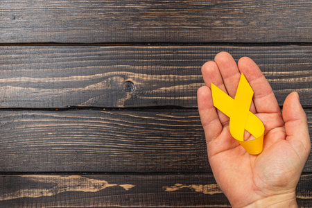 A woman holds a yellow awareness ribbon in her hand, representing the fight against cancer and hope for those affected. The background features wooden textures.の写真素材