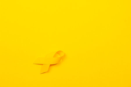Hands hold a yellow ribbon against a bright background, representing courage and support for cancer awareness and treatment. This symbolizes the fight against illness and solidarity.の写真素材