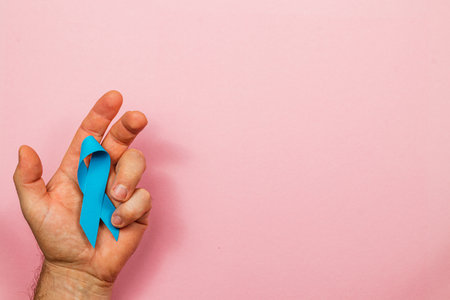 A male hand displays a blue ribbon on a pink background, highlighting awareness for cancer causes. This visual conveys hope and support for patients and their families.の写真素材