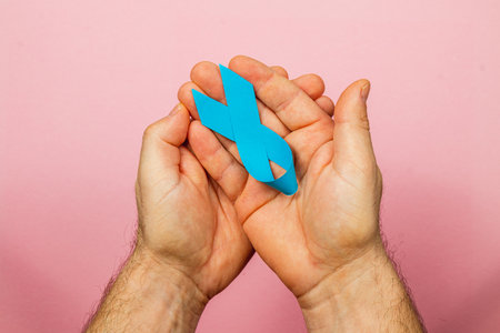 A male patient holds a blue ribbon symbolizing cancer awareness and prevention against a soft pink background. This symbolizes hope and support for those affected by cancer.の写真素材