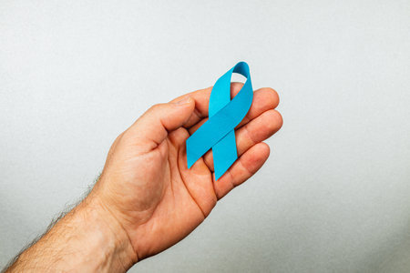 A male hand holds a blue awareness ribbon, symbolizing support for cancer detection and prevention. This simple yet powerful gesture promotes hope and courage in the fight against illness.の写真素材