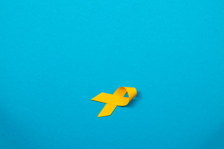 A yellow ribbon lays on a vibrant blue background, signifying awareness and support for cancer patients and survivors. This symbol embodies hope and the fight against illness.の写真素材