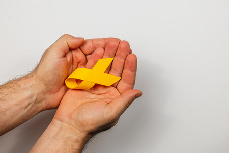 Two hands gently hold a yellow ribbon, representing awareness and support in the battle against cancer. This symbol emphasizes hope and solidarity for those affected by the illness.の写真素材
