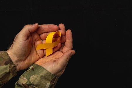Two hands gently hold a yellow ribbon, symbolizing support and awareness for cancer. The background is dark, highlighting the message of hope and solidarity in the fight against illness.の写真素材