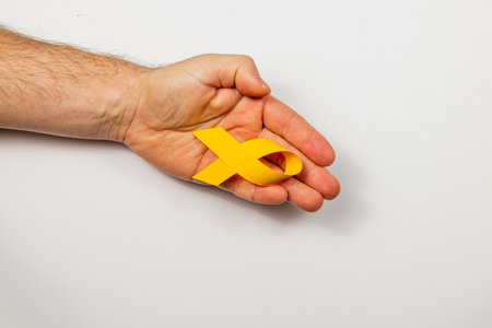 A female hand holds a yellow ribbon, symbolizing support for cancer awareness. This represents the fight against illness and emphasizes the importance of solidarity and care.の写真素材