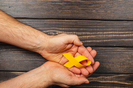 Two hands gently cradle a yellow ribbon symbolizing support for cancer awareness. This represents solidarity and hope for those affected by illness and encourages early detection.の写真素材