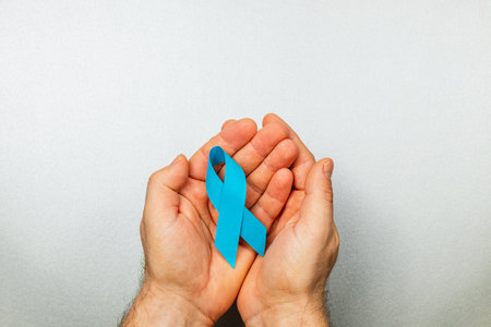 Two hands gently cradle a blue ribbon, symbolizing hope and support for cancer awareness, reflecting a strong commitment to detection and treatment efforts in healthcare.の写真素材
