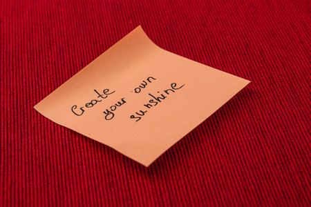 A simple sticky note rests on a vibrant red surface with an uplifting message written in black ink, promoting the idea of creating personal happiness and positivity.の写真素材