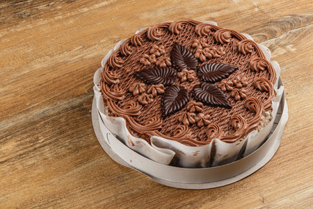 A beautifully crafted chocolate cake is displayed on a rustic wooden table. The cake features intricate frosting designs and decorative chocolate leaves, inviting dessert lovers.の写真素材