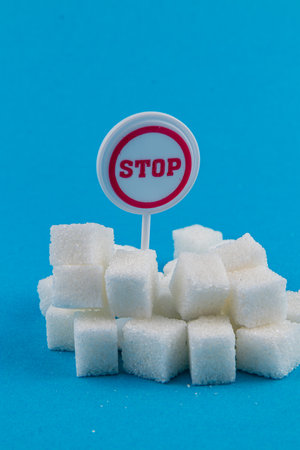 A pile of white sugar cubes is displayed against a bright blue background. A red and white stop sign is placed in the center, suggesting a warning about excessive sugar intake.の写真素材