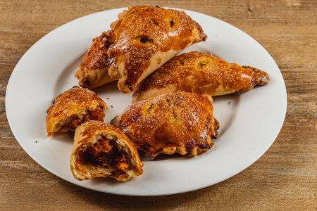 Golden-brown pastries filled with pumpkin sit on a white plate. The flaky crust reveals rich pumpkin filling, ready to be enjoyed as a savory snack or dessert at a cozy gathering.の写真素材