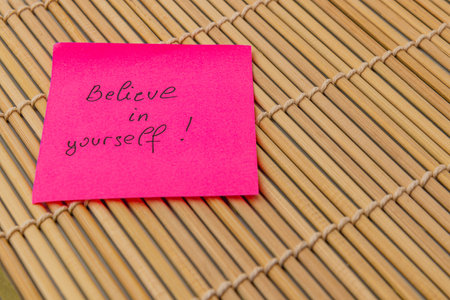 A pink sticky note with the message 'Believe in yourself!' is placed on a bamboo mat, conveying an encouraging message of self-confidence and motivation.の写真素材