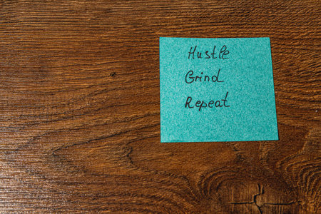 A bright turquoise sticky note is placed on a wooden table, featuring handwritten words that inspire dedication and perseverance.の写真素材