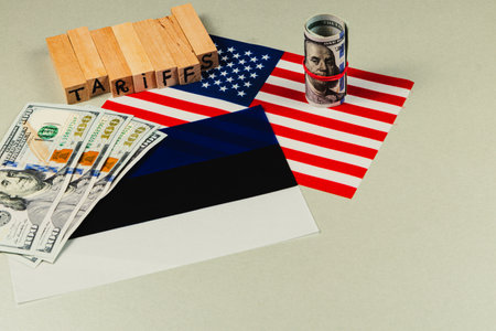 Flags of USA and Estonia are displayed alongside stacks of dollars and blocks spelling tariffs, highlighting political and economic negotiations in trade.の写真素材