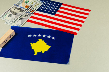 Flags of the USA and Kosovo lie on a table alongside cash, reflecting the economic implications of tariffs, trade negotiations, and international politics.の写真素材
