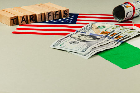 Wooden blocks spell tariffs next to a US flag and stacks of cash. The focus highlights economic factors influencing trade and policy decisions in modern politics.の写真素材