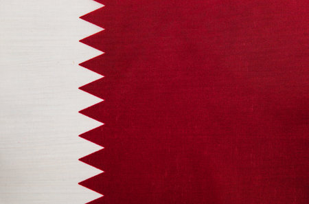 The flag of Qatar is shown with its distinctive maroon and white colors, featuring a serrated...