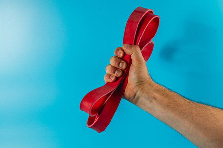 A hand firmly grips a vibrant red rubber band against a bright blue backdrop, showcasing a playful and dynamic visual with a simple yet striking contrast.の写真素材