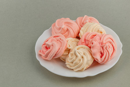 A collection of pink and white meringue cookies sits on a round white plate, showcasing a delightful treat perfect for dessert lovers or special occasions.の写真素材