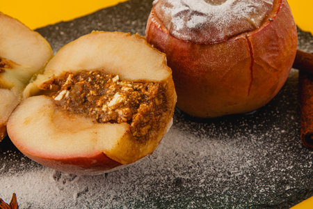 Baked apples filled with a rich caramel mixture sit on a dark slate plate, sprinkled with powdered sugar, and surrounded by cinnamon sticks, creating a cozy atmosphere.の写真素材