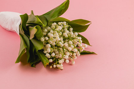 A bouquet of white flowers with green leaves rests gently on a pastel pink surface, creating a serene and elegant visual display fit for any occasion.の写真素材