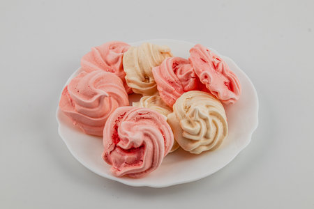 Colorful meringues in pink and cream are arranged on a white plate, showcasing their swirled designs. Perfect for dessert or a sweet treat at any gathering.の写真素材