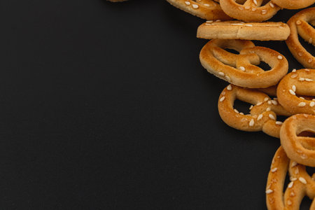 Savory pretzels with a golden-brown hue and sesame seeds are casually scattered across a black surface, perfect for enjoying as a snack or party treat regardless of the occasion.の写真素材