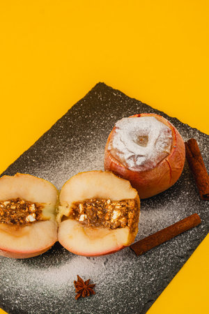 Two baked apples sit on a dark slate surface. One apple is sliced in half, revealing a sweet filling...