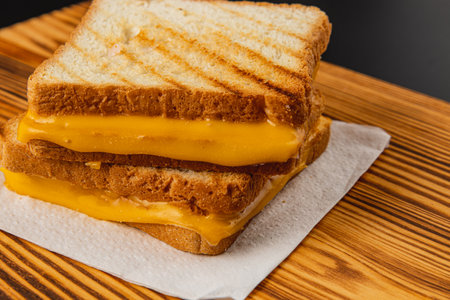 A perfectly grilled cheese sandwich, featuring golden melted cheese between crunchy toasted bread slices, rests on a wooden board ready to be enjoyed for breakfast or lunch.の写真素材