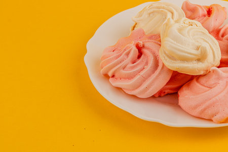 A plate holds an assortment of pink and white meringue cookies, showcasing a delightful texture and color against a vibrant yellow background.の写真素材
