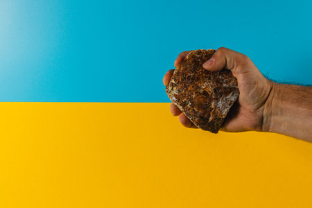 A hand grips a textured rock firmly while positioned against a vibrant blue and yellow backdrop that creates a striking visual contrast during daytime.の写真素材